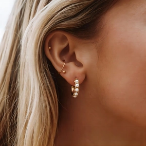 Gros plan de boucles d'oreilles dorées en C serties de perles et de clous assortis