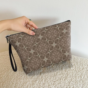 Brown geometric cosmetic bag with zip closure and wrist strap held in hand for travel