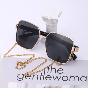 Detailed close-up of large frame sunglasses with gold metal chain temple and dark lenses