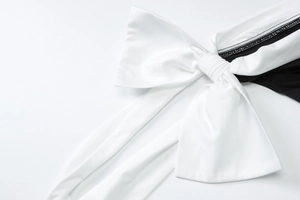 Detail of a large white decorative bow on a black slim fit dress with smooth texture
