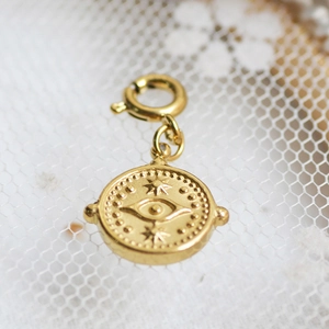 Macro detail of gold round pendant with Evil Eye embossing and spring clasp on lace