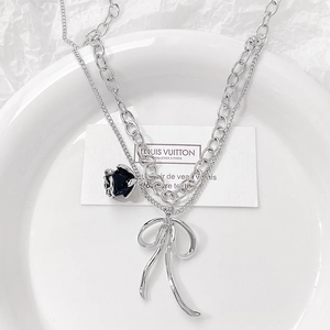 Silver layered necklace with black rose and metal bow charms in a cool industrial style