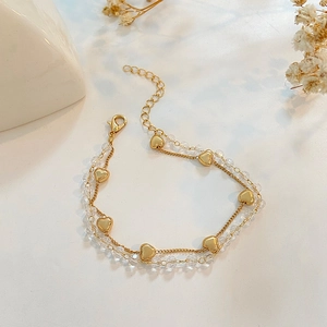 Pulsera de doble capa dorada con corazones y cuentas de cristal sobre fondo blanco