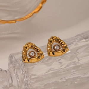 Detail of hammered triangle gold stud earrings with white pearl inlay on glass surface