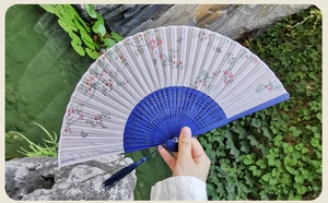 Detail of silk folding fan with pink peach blossoms and butterfly in a Chinese garden