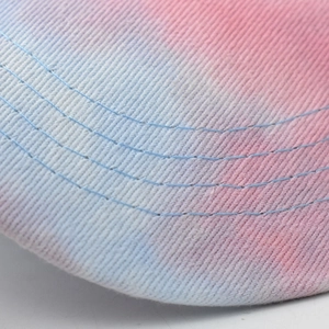 Detailed close-up of a tie-dye visor brim featuring pink and blue cotton twill stitching