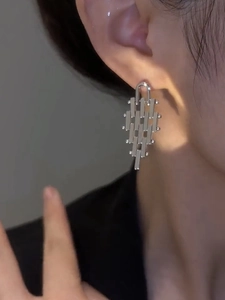Macro shot of silver geometric trapezoid metal earrings on ear with high-gloss finish