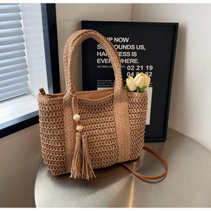 Detailed close-up of straw woven tote bag featuring hollow texture and tassel charm detail