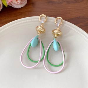 Détail de boucles d'oreilles feuille avec goutte bleue et anneaux pastel entrelacés