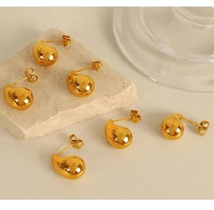 Detailed view of polished gold teardrop earrings on a beige stone surface