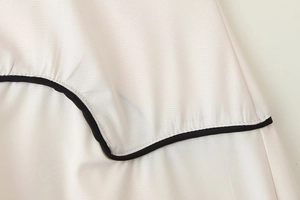 Gros plan d'une robe sans manches beige avec liseré noir sur les coutures courbes