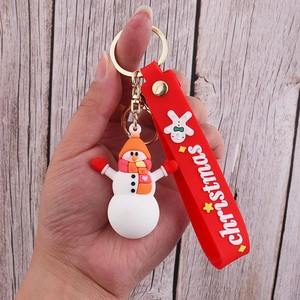 Close-up of PVC snowman keychain with red strap being held over a wooden floor