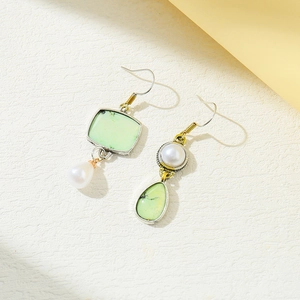 Detail of vintage asymmetric earrings featuring light green stones and white pearls