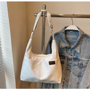 Detail of cream nylon tote with side pocket, fashion label, and adjustable strap on a rack