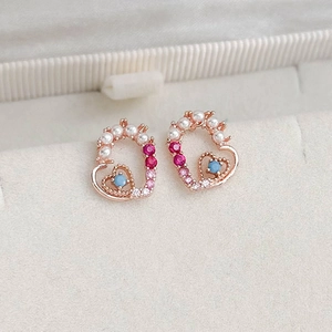 Detailed macro of rose gold heart stud earrings with zircons and pearls on beige velvet
