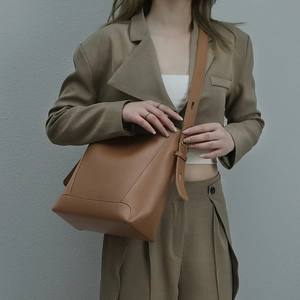 Fashionable brown leather bucket bag with adjustable strap worn by a model in a suit