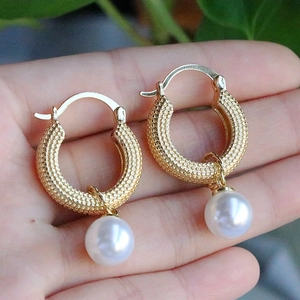 Close-up of golden textured hoop earrings with large white pearls held in palm