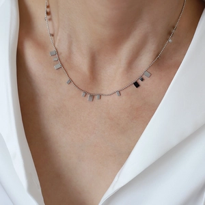 Detail of silver beaded necklace with polished square pendants on a white shirt