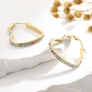 Close-up of golden heart hoop earrings with colorful rhinestones on a stone background