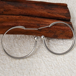 Detailed view of silver stainless steel hoop earrings with ball ends on wooden decor