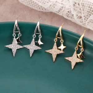 Elegant gold and silver star earrings with cubic zirconia on a green display