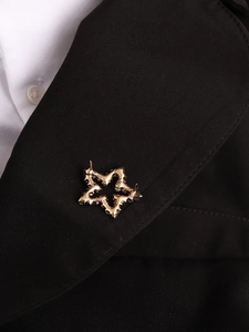 Detailed close-up of a gold star brooch with textured surface on a black suit lapel