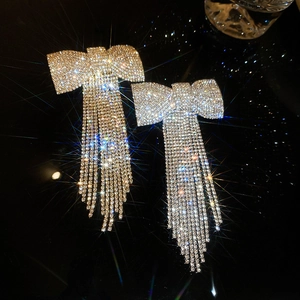 Boucles d'oreilles nœud argenté avec de longs glands en strass sur fond noir brillant