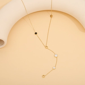 Minimalistische goldene Y-Halskette mit schwarz-weißen runden Muschelanhängern auf beigem Grund