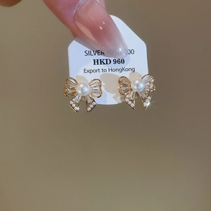 Detailed macro of bow-shaped pearl earrings with sparkling cubic zirconia in gold finish