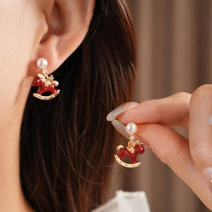 Detailed close-up of golden rocking horse earrings with red enamel and white pearl accents