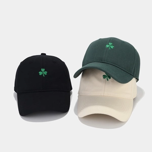 Détail de la broderie trèfle sur des casquettes en coton noir, beige et vert foncé