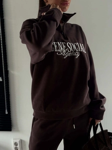 Detail of embroidered lettering on brown half-zip sweatshirt with high collar