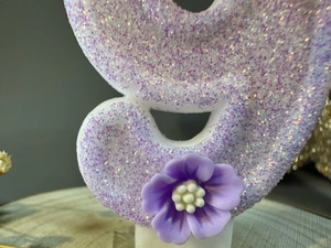 Macro shot of purple glitter candle surface featuring a small decorative flower detail