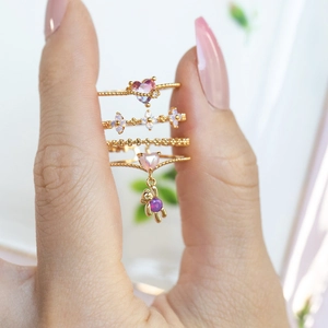 Golden rings set with pink heart gems, purple floral accents, and a dangling bear charm