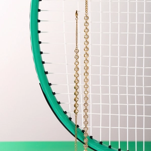Detailed shot of golden tennis bracelet and zircon necklace on tennis racket strings