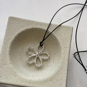 Detail of silver beaded flower pendant with black cord on stone tray background