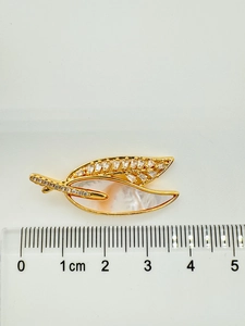 Detailed view of a gold leaf brooch with zircon crystals and mother of pearl on a ruler