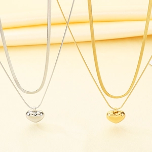 Detail of layered gold and silver snake chains with 3D heart pendants and polished finish
