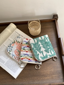 Three-piece linen coin purse set with floral embroidery on a vintage wooden tray