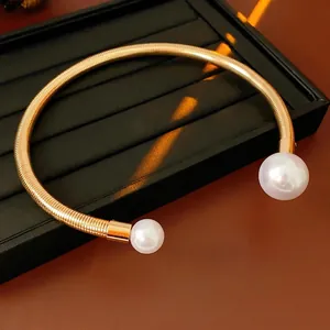 Elegant gold spiral metal choker necklace with two large pearls on a display