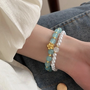 Detail of a 2-piece set of vintage flower glass and faux pearl beaded bracelets on wrist