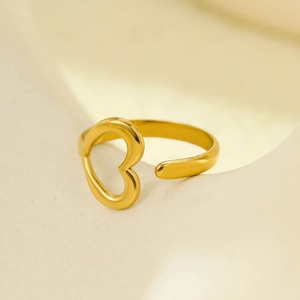 Detail of 18K gold-plated open ring with hollow heart design on a beige display stand