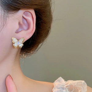 Detailed close-up of a 18k gold butterfly earring with white enamel and a central gem