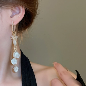 Gros plan de boucles d'oreilles à pampilles dorées avec pétales de nacre sur modèle