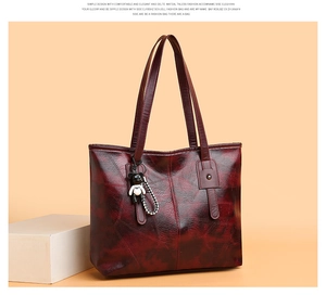 Detail of dark red PU leather tote bag with wax texture and a cute black bear charm