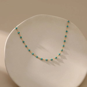 Minimalist 18K gold plated necklace with turquoise beads on a beige ceramic plate