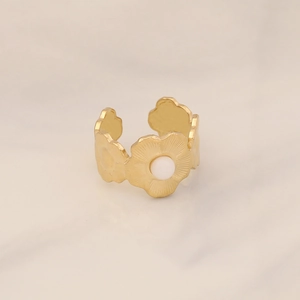Detail of gold flower shaped open ring with a central white pearl on marble background