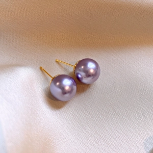 Close-up of elegant purple pearl earrings on a beige silk fabric background