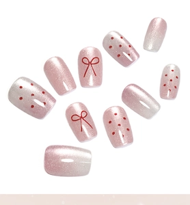 Detail of pink cat-eye press-on nails with red bow designs and polka dot accents
