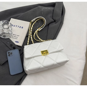 Detailed view of a white quilted chain bag with a gold lock on a grey blazer background
